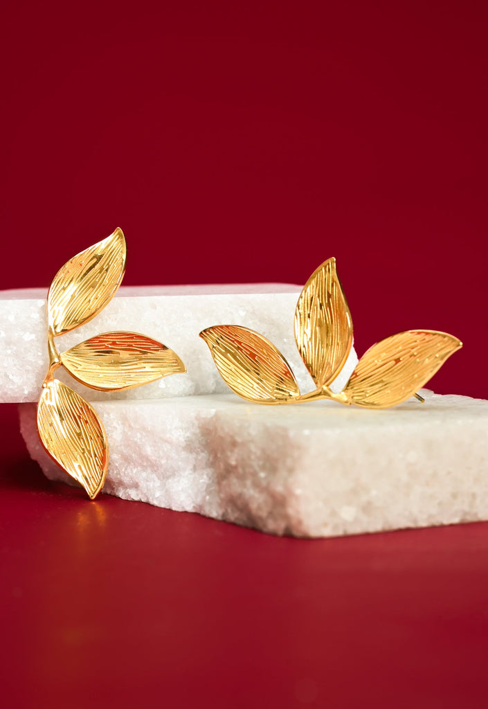 Gold leaf-shaped earrings on a red and white background