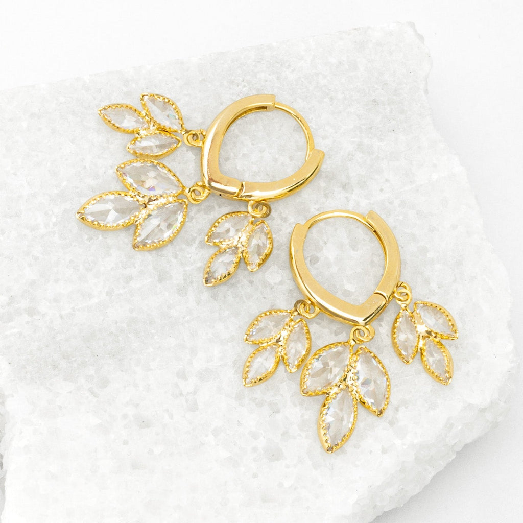 Gold earrings with leaf-like designs on a white textured surface