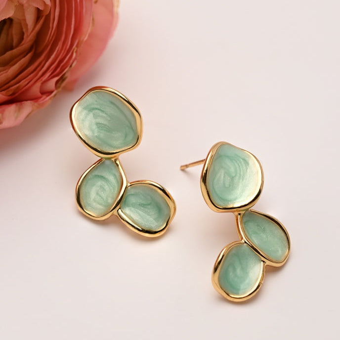 Gold earrings with green stones on a light pink background