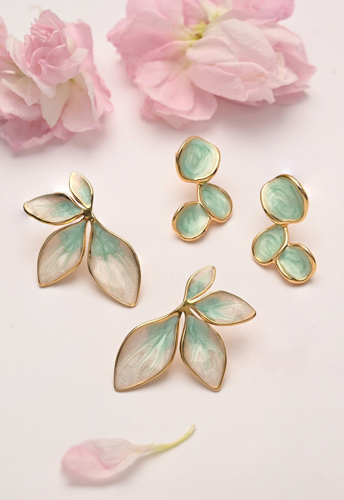 Pair of gold and green earrings on a light pink background with pink flowers.