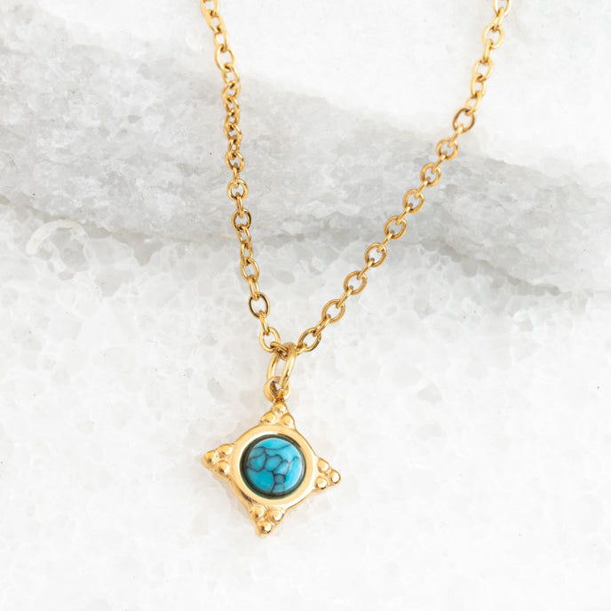 Gold necklace with a turquoise pendant on a marble background