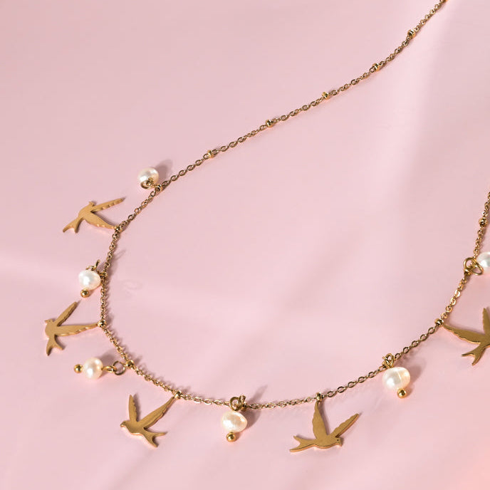 Necklace with bird and pearl charms on a pink background
