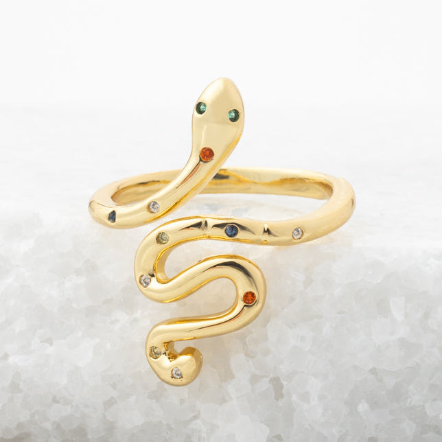 Gold snake-shaped ring with gemstones on a light gray background