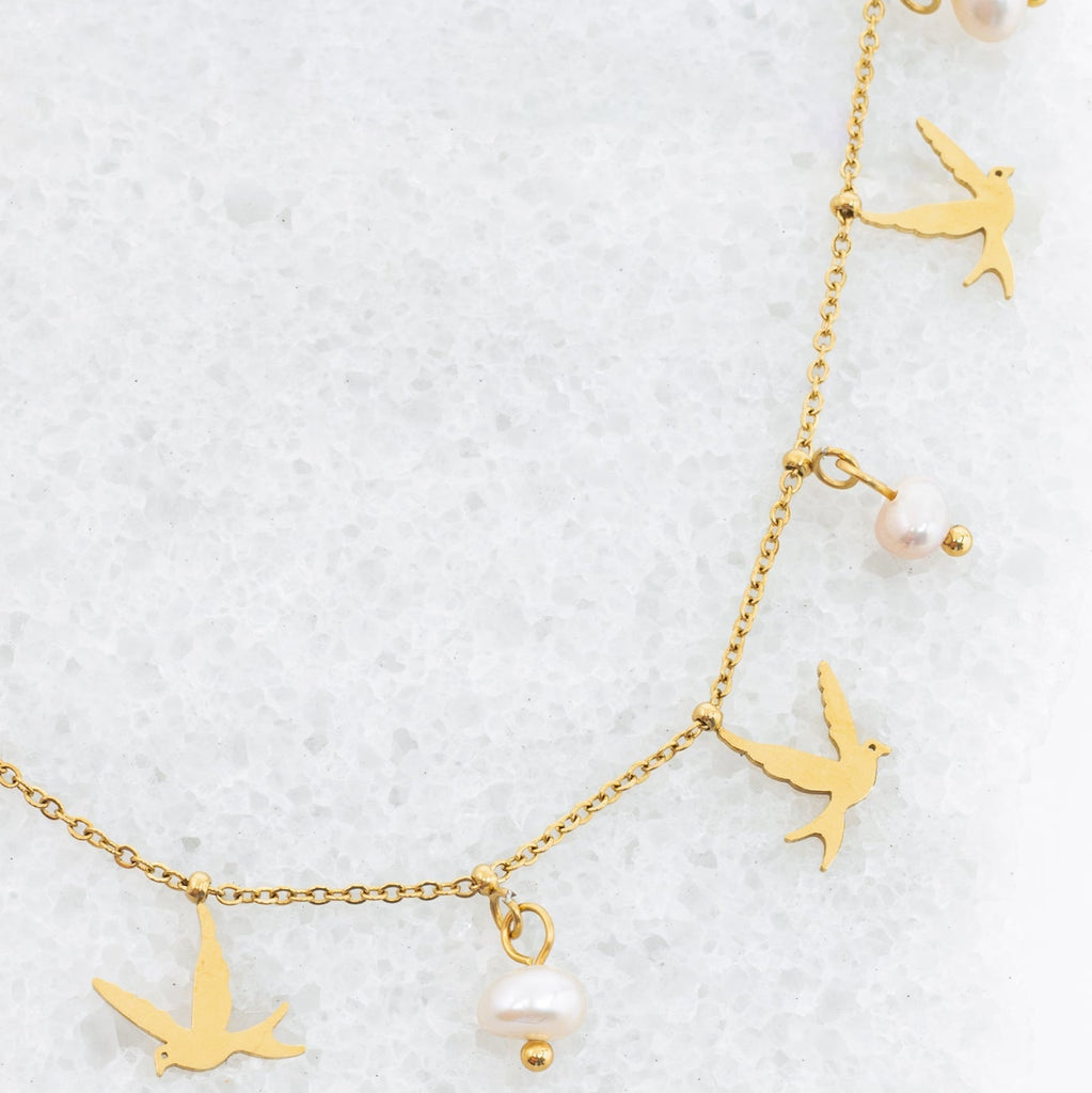 Gold necklace with bird and pearl charms on a white background