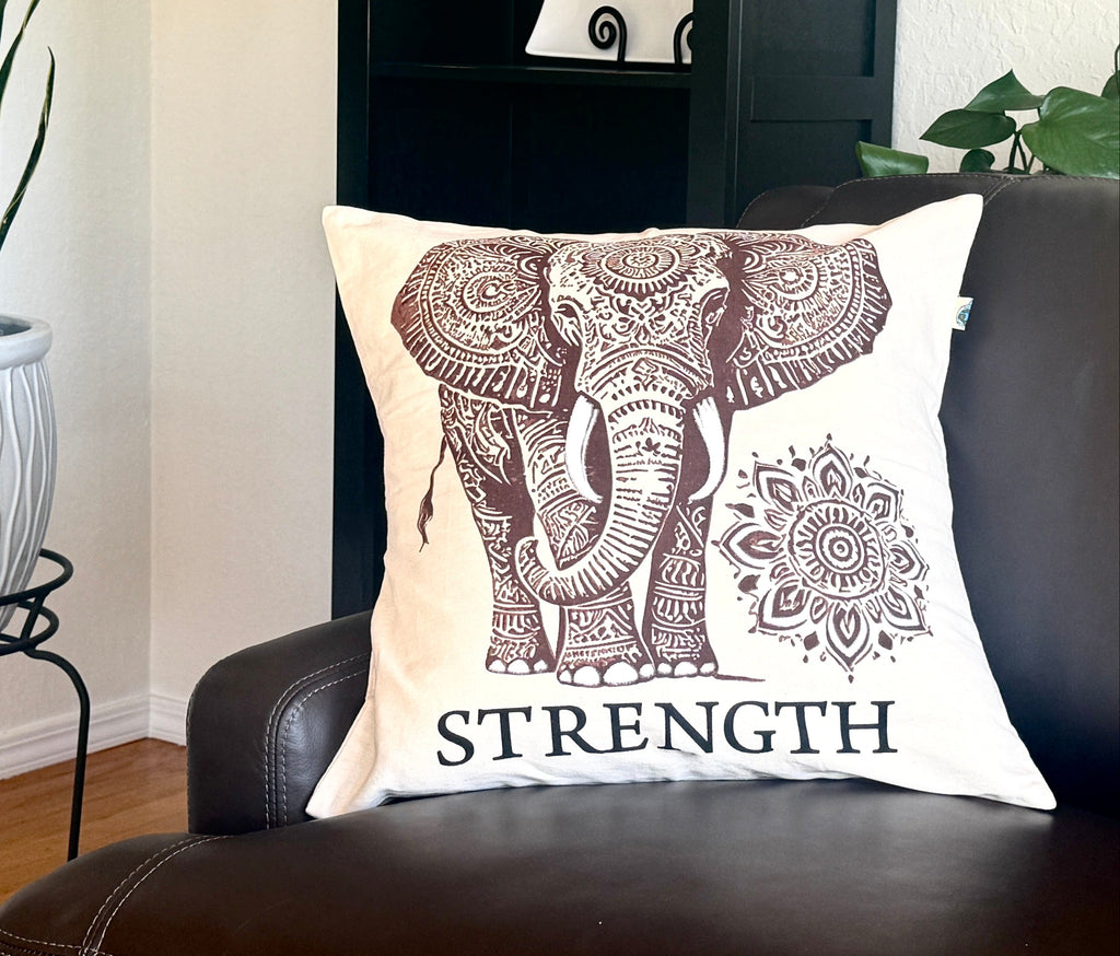 Decorative pillow with elephant design and 'STRENGTH' text on a brown leather couch.